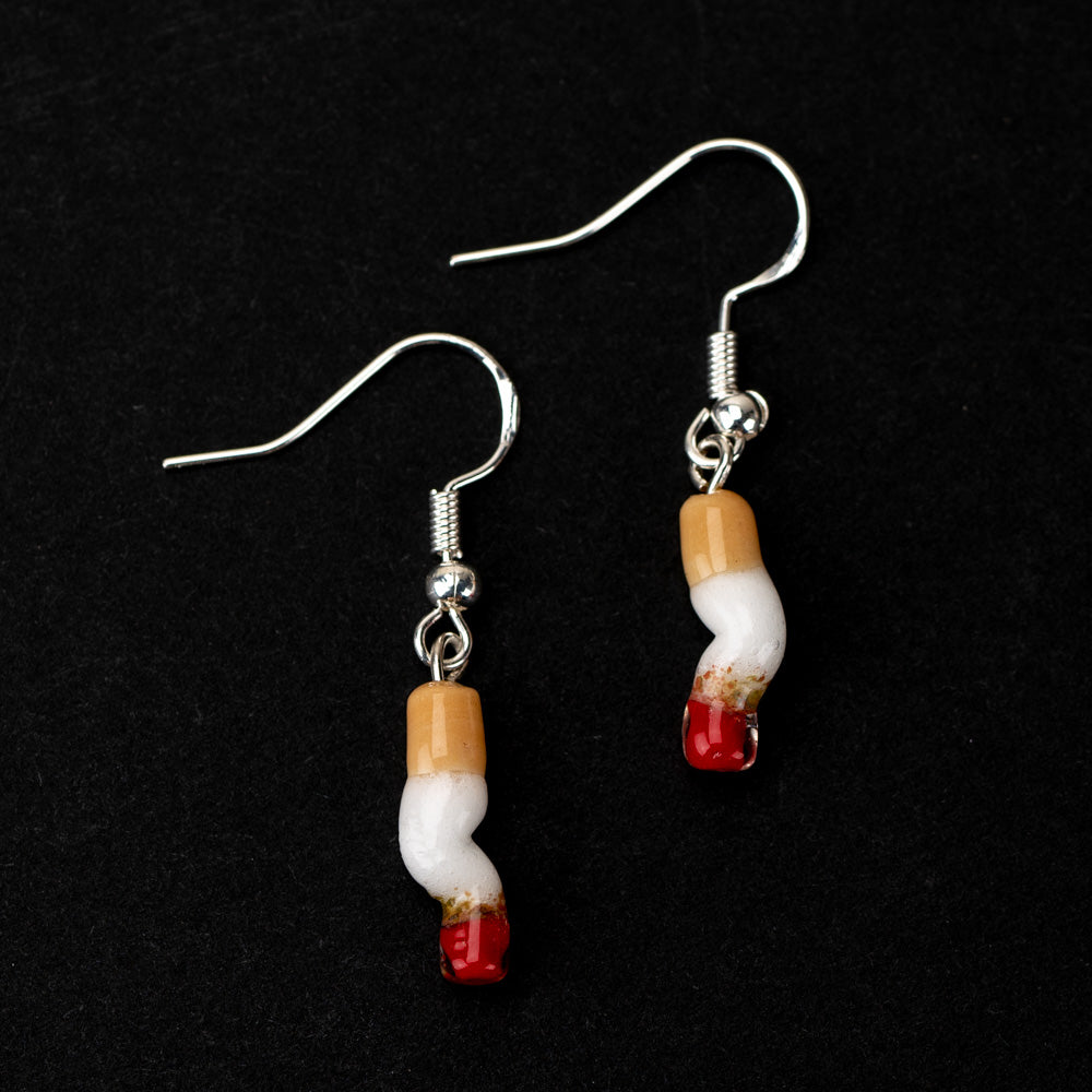 Two cigarette shaped earrings with silver dangle backings on a black background. The cigarettes are made of glass and resemble a smashed cigarette.