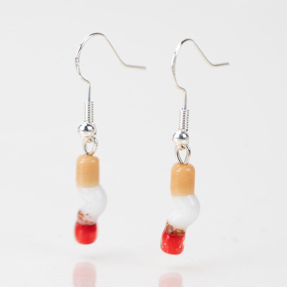 Two cigarette shaped earrings with silver dangle backings on a white background. The cigarettes are made of glass and resemble a smashed cigarette. 