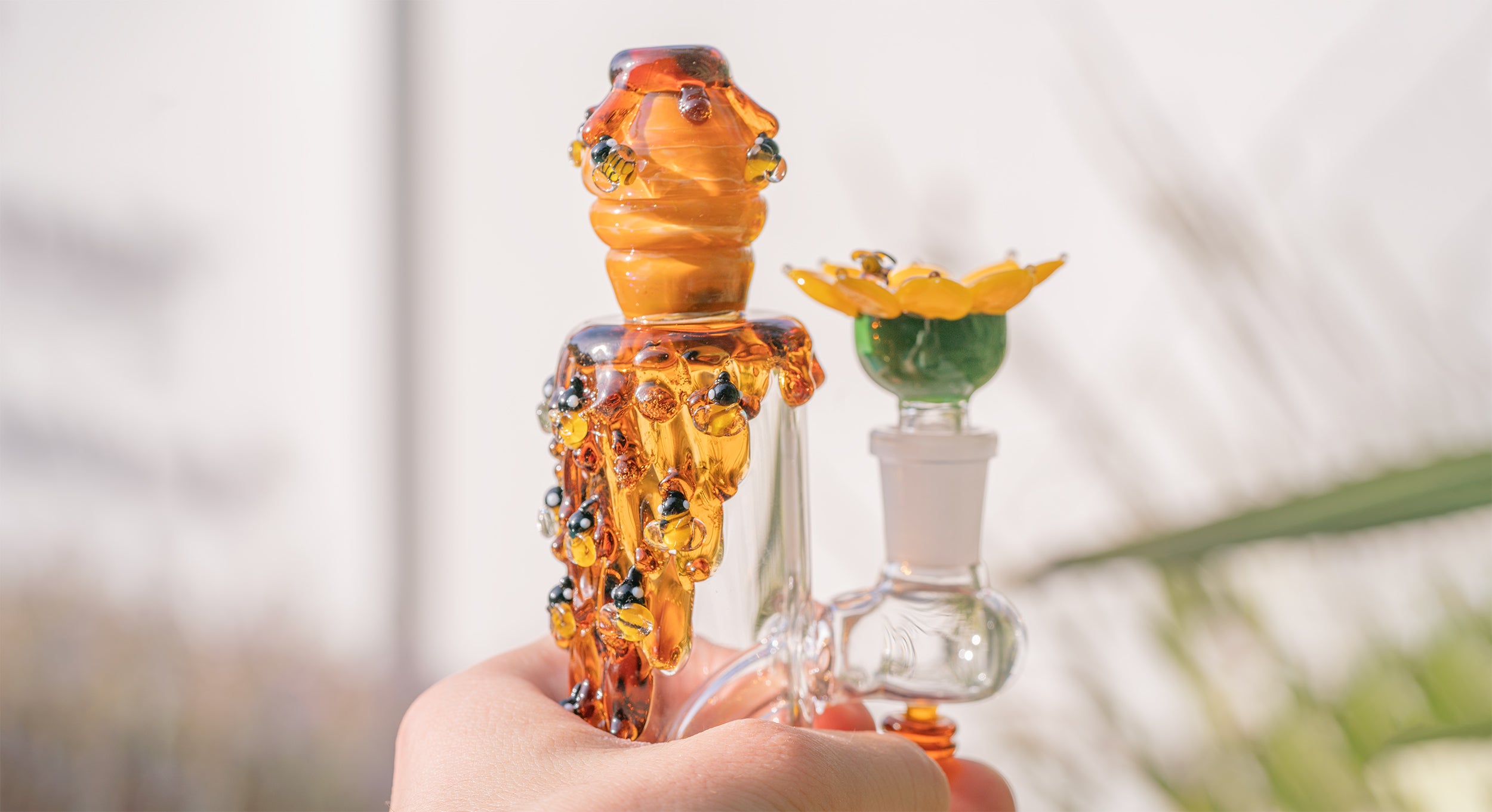 Glass smoking device with intricate design held by a hand against a blurred background