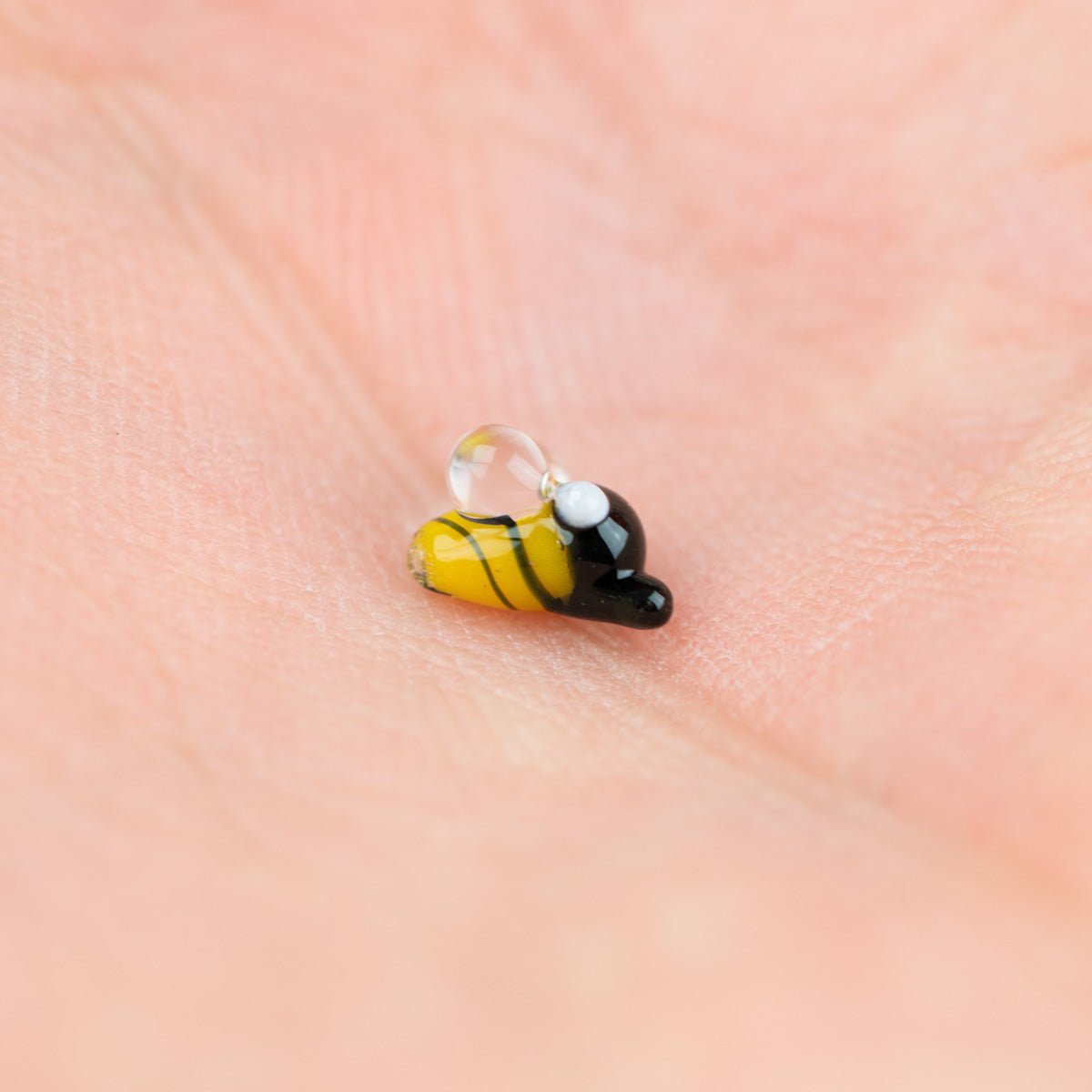 Small yellow and black bee-shaped pearl on a person's palm.
