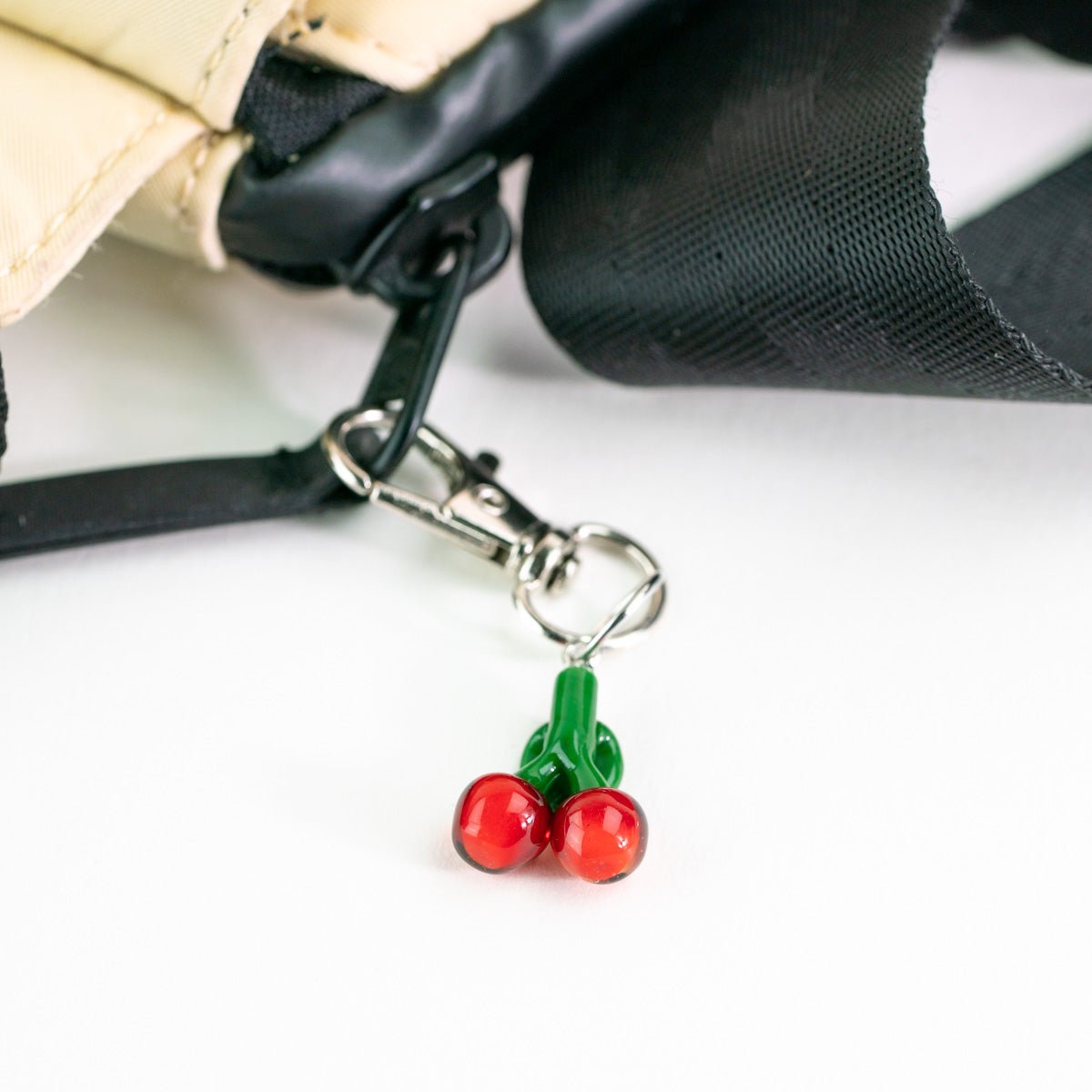 Cherry-shaped keychain attached to a black strap on a white background