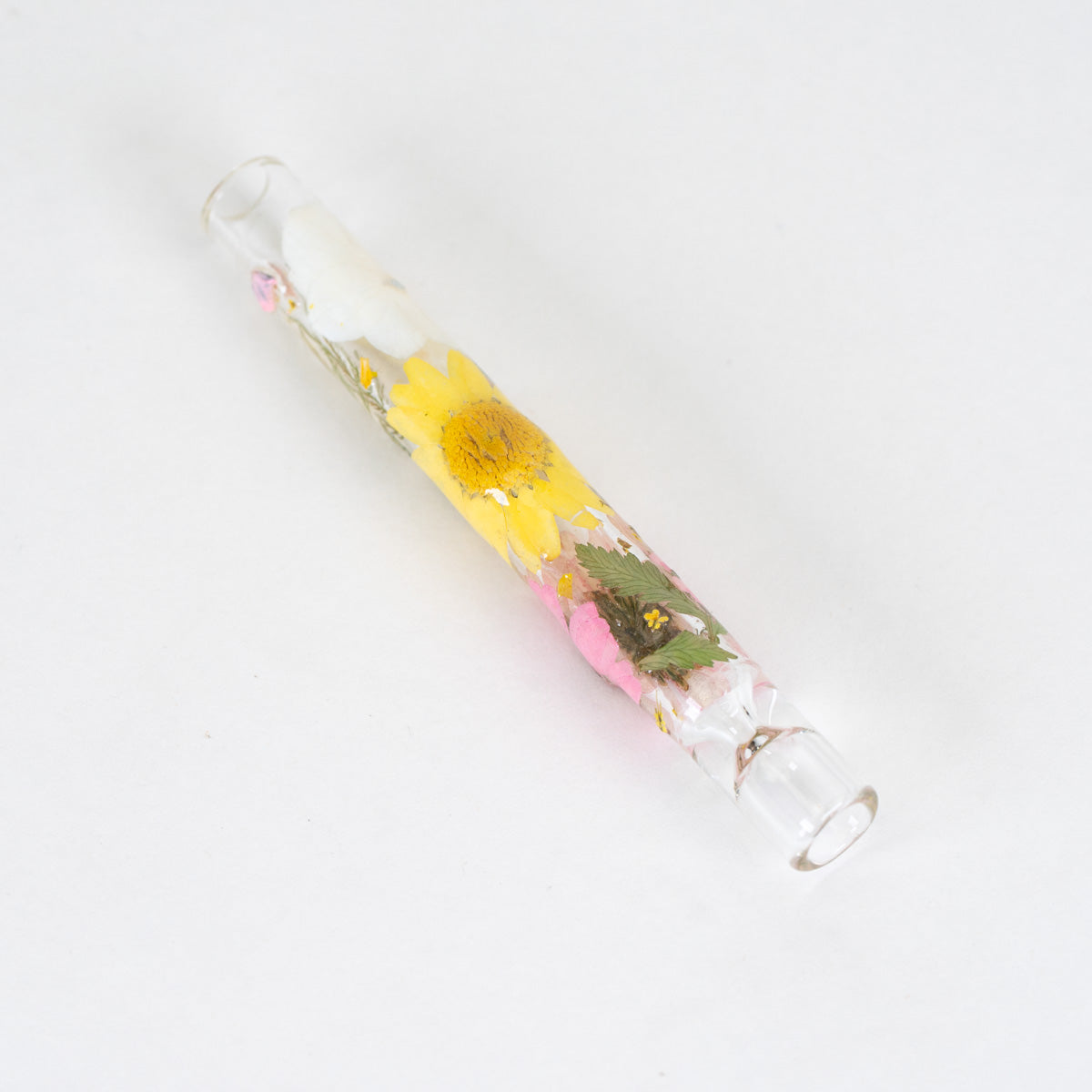 A clear glass tube with a glass bottom, containing a preserved yellow sunflower and pink flowers in clear resin, photographed on a white background.