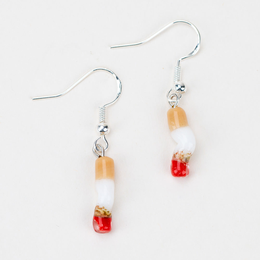 Two cigarette shaped earrings laying flat on a white background. The earrings are made of glass and look smashed.  