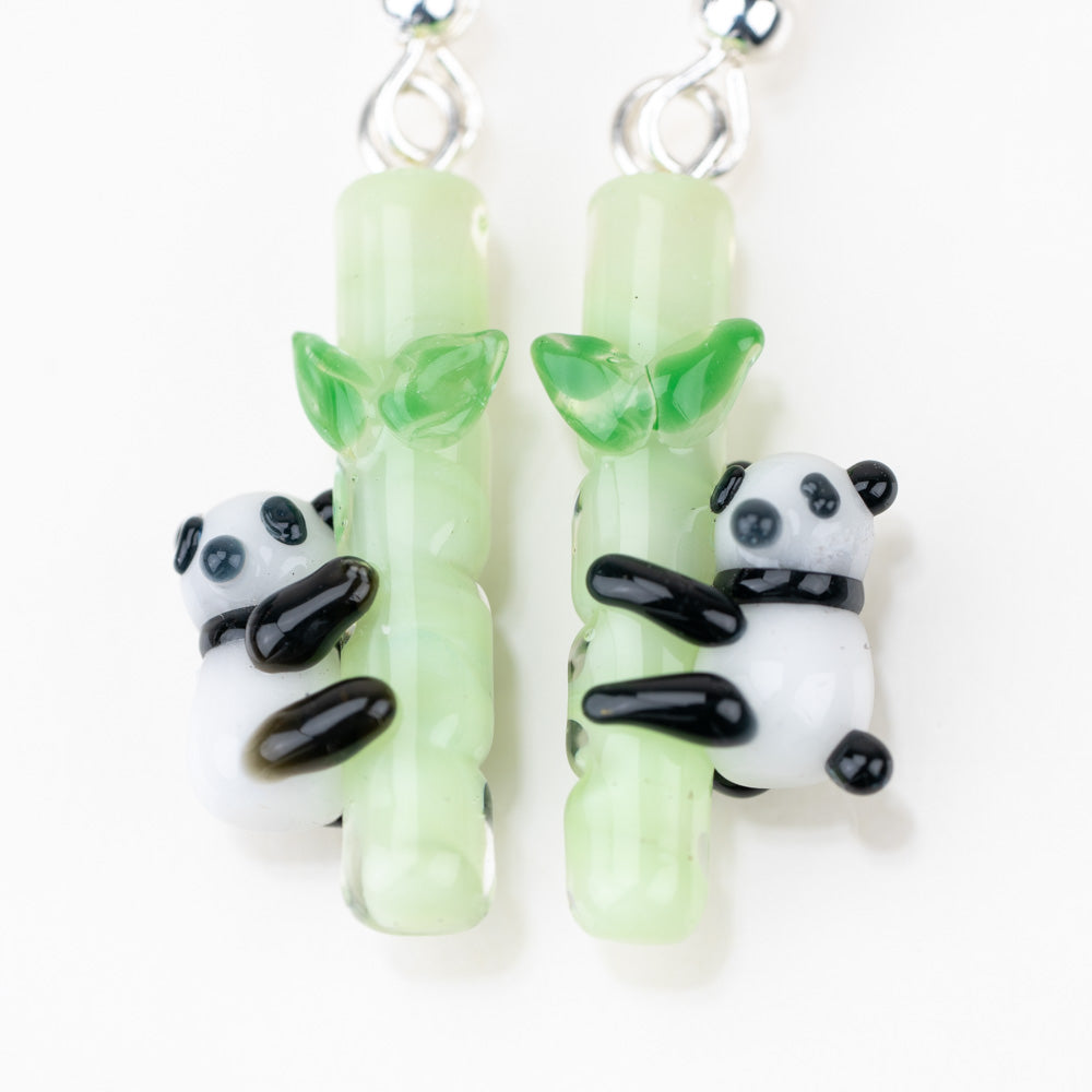 A close up of the Panda Love earrings featuring two pandas hugging a bamboo pole. The bamboo is green and the pandas are black and white. 