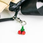 Cherry-shaped keychain attached to a black strap on a white background
