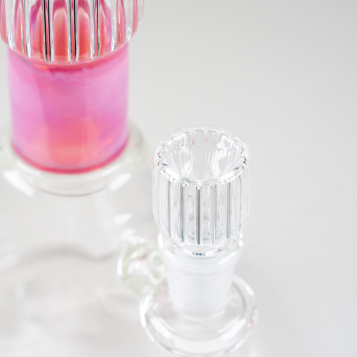 Angled close-up of the matching clear ribbed glass bowl with the Rosaline Beaker's pink neck accent in the background
