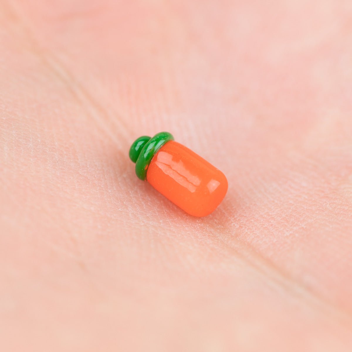 Small orange and green Sriracha bottle terp pearl on a person's palm