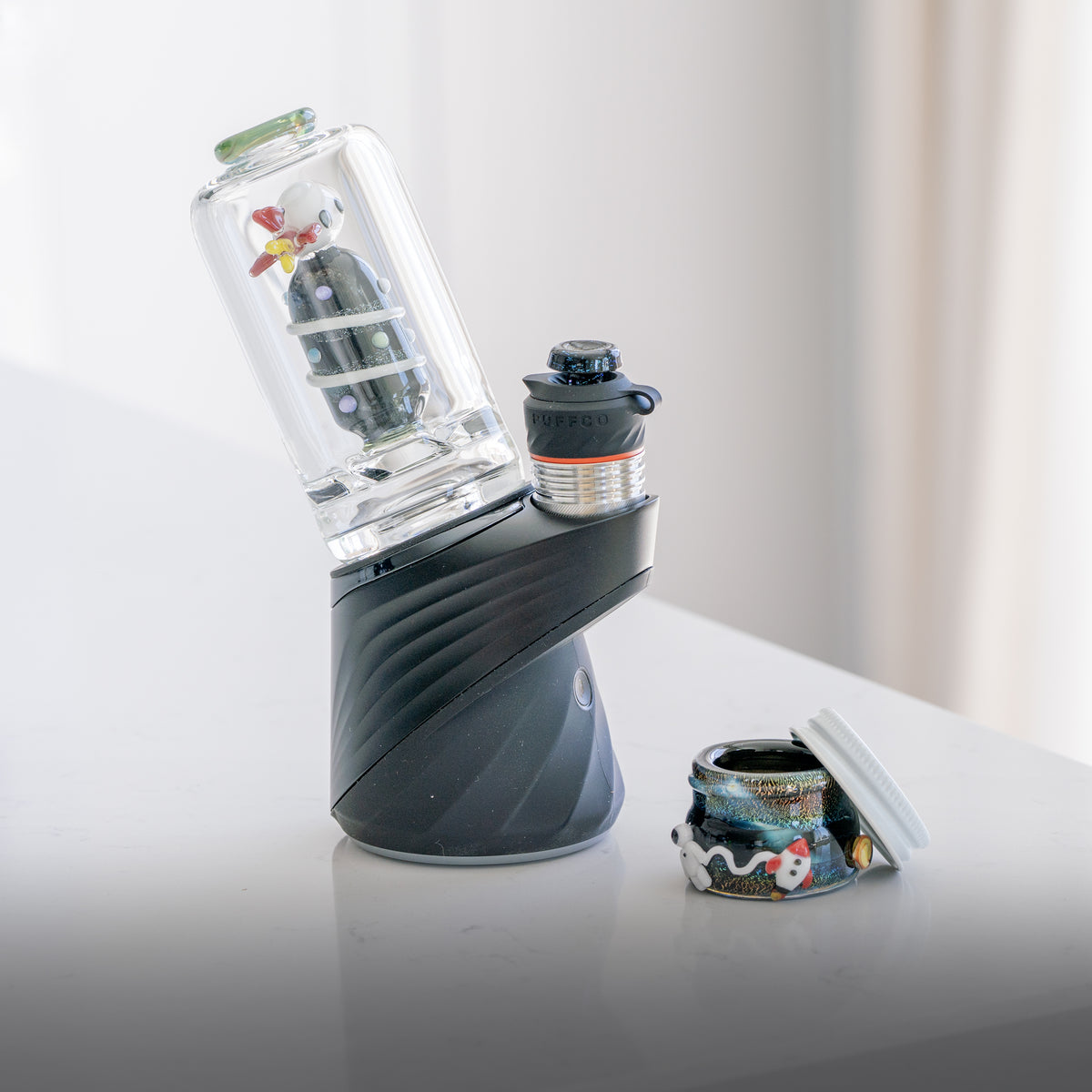 A Puffco Peak Pro with a rocketship themed glass attachment and a space-themed glass terp jar by Empire Glassworks