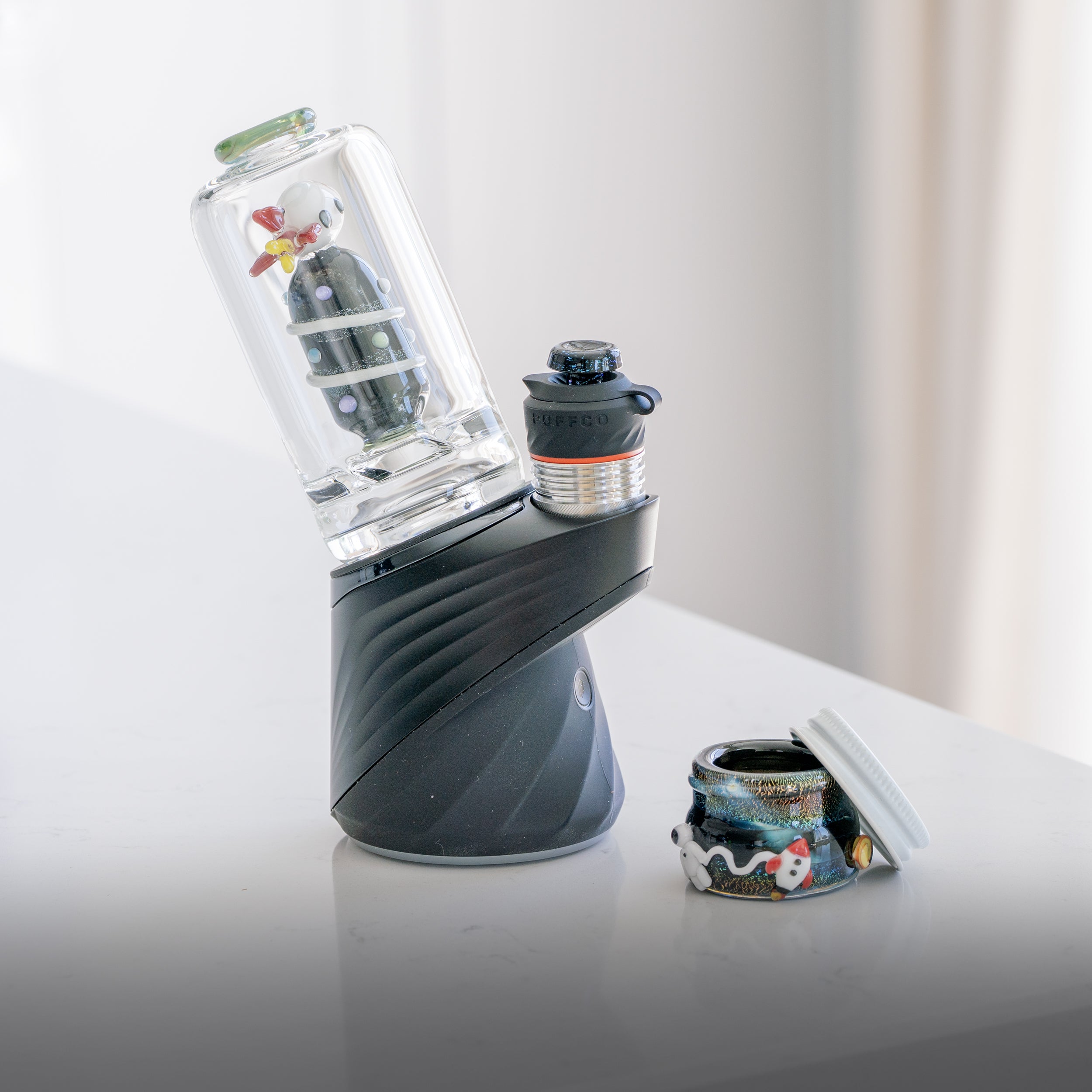 A Puffco Peak Pro with a rocketship themed glass attachment and a space-themed glass terp jar by Empire Glassworks