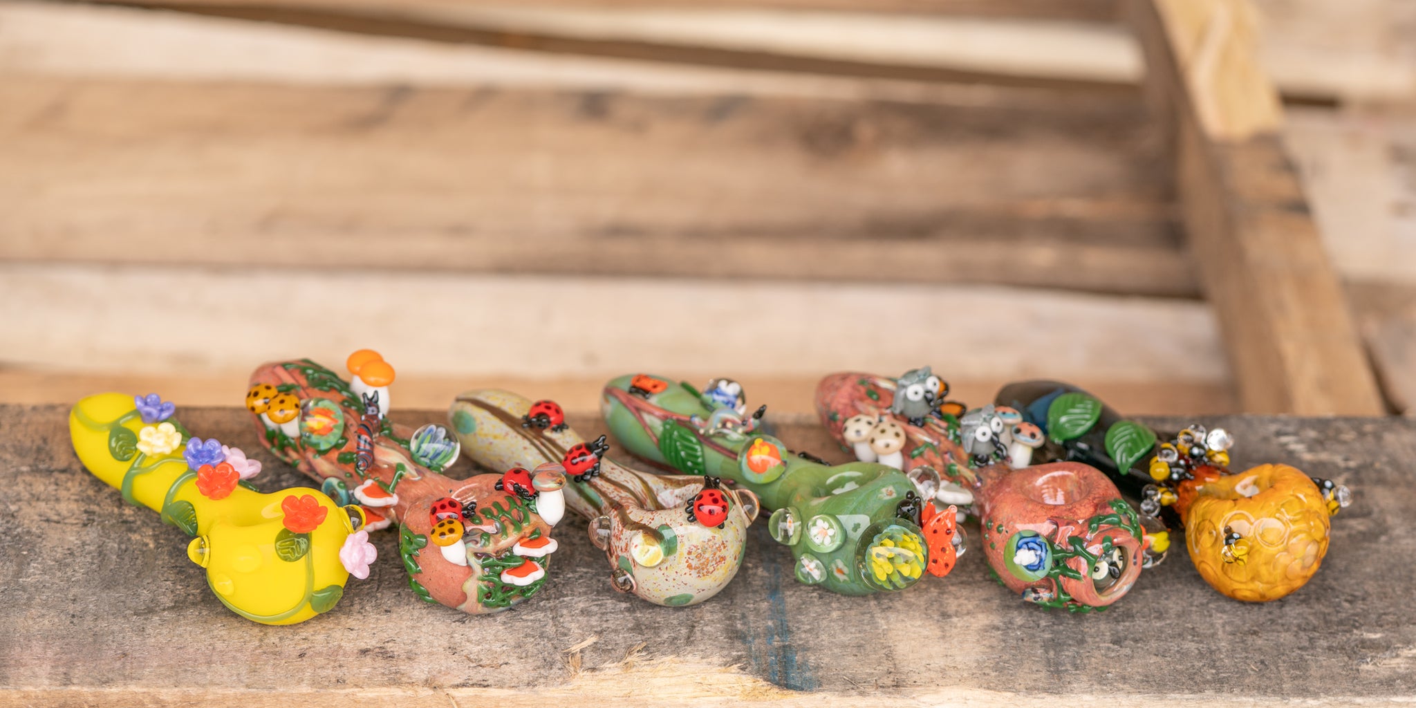 An assortment of six different glass spoon pipes, featuring Beehive, Hootie's Forest, Garden Critters, Lady Bugs, Bug's Life, and Sunshine Garden