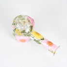 A clear glass water pipe decorated with pressed pink flowers, green leaves, and yellow accents, shown on a plain white background.