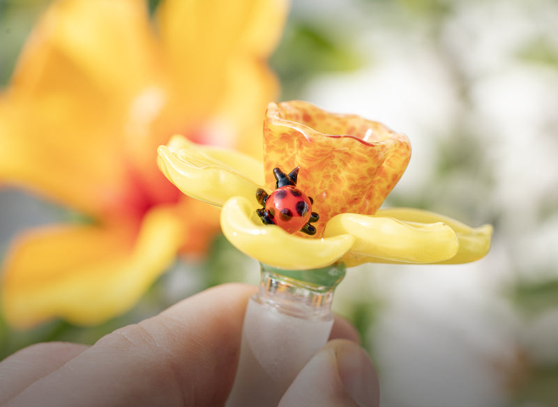 A hand holding a glass flower bowl piece with a sculpted lady bug made by Empire Glassworks