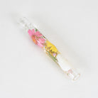A clear glass smoking pipe containing pressed flowers, including pink and yellow blossoms, set against a plain white background.
