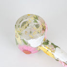 A clear glass smoking pipe decorated with pressed flowers in pink, yellow, white, and green, featuring gold foil lettering that reads 'Moonray x Empire' on a plain white background.
