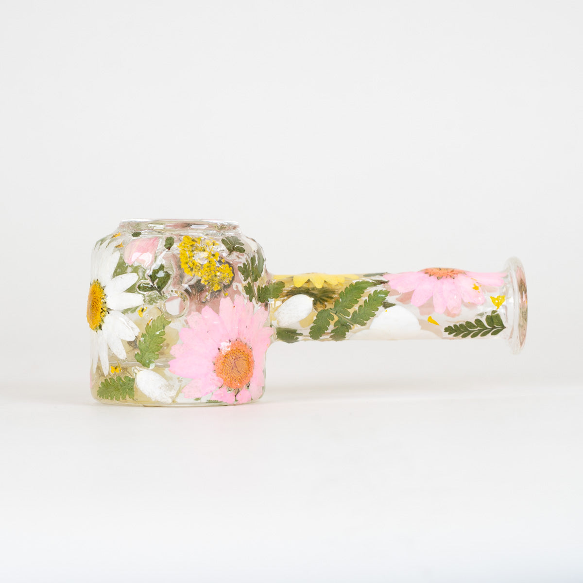 Glass spoon pipe consisting of white, pink, and yellow flowers on a white background