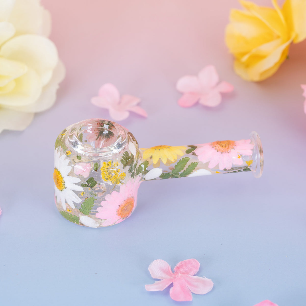 Decorative glass spoon pipe with decorative pink, yellow, and white flowers on a blue and pink background