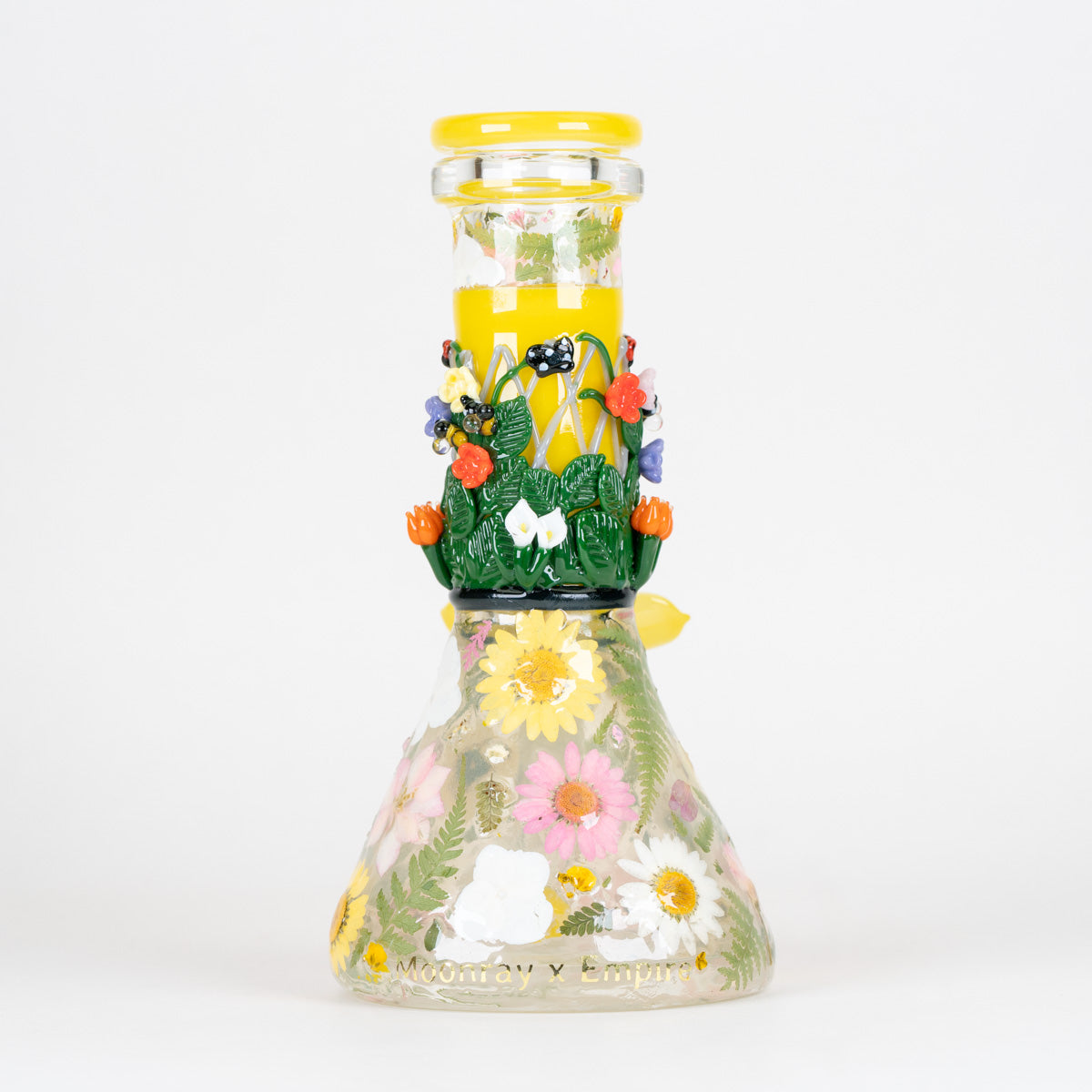 A clear glass beaker with decorative glass pieces and pressed flowers