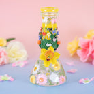 A decorated glass beaker with pressed flowers embedded