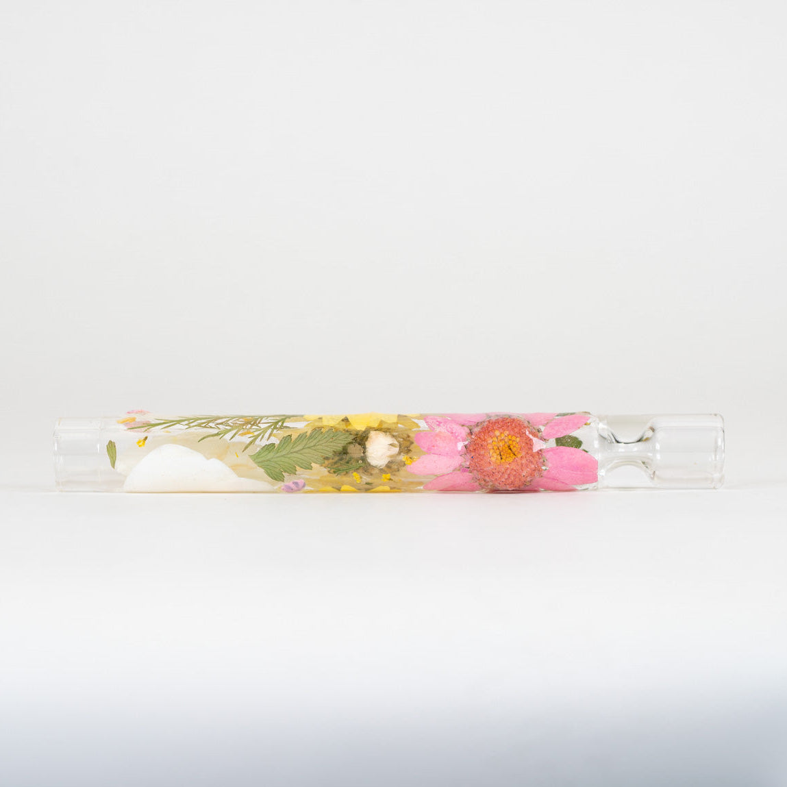 A clear glass chillum with decorative pressed flowers on a white background