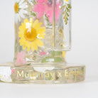 A close-up of a clear glass banger with pressed floral decals, including a prominent yellow daisy and pink flowers, and gold foil text reading 'Moonray x Empire' on the base, set against a plain white background.