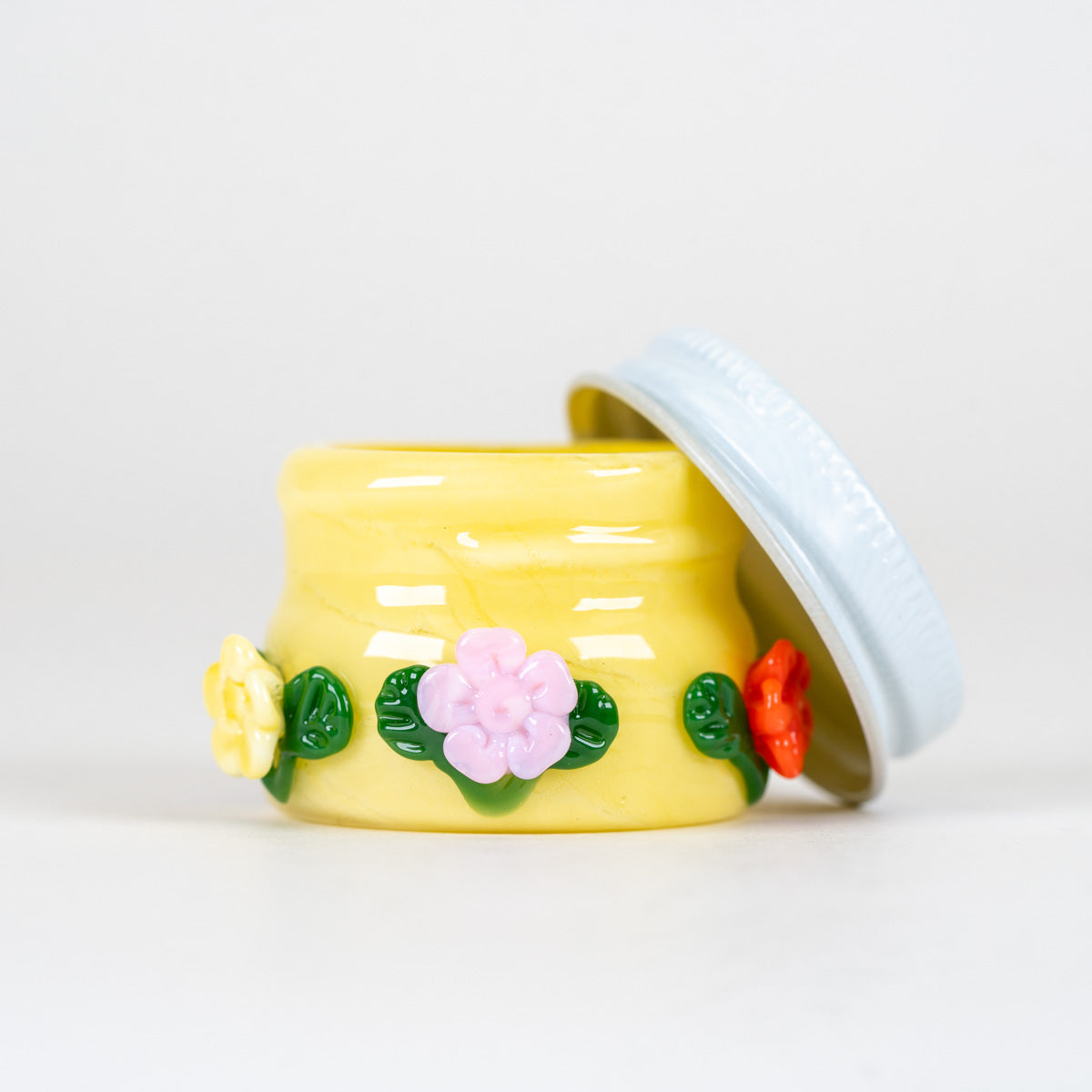 A small yellow glass container with pink, red, and yellow flowers for dabbing and smoking
