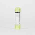 A clear cylindrical glass container with a translucent light green cap and base, featuring a black printed graphic and a white iridescent figure inside, set against a plain white background.