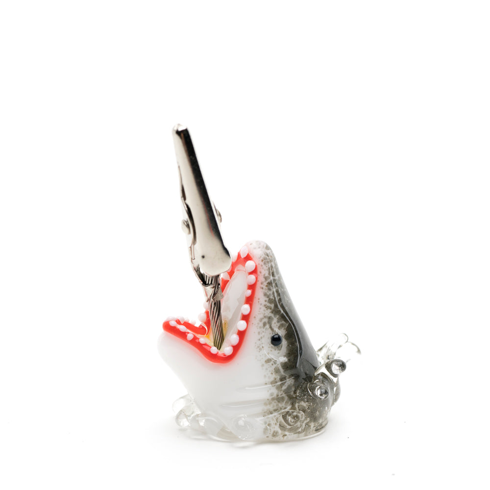 A roach clip shaped like a shark emerging from the ocean. The joint holder is placed in the midst of the shark's jaws.